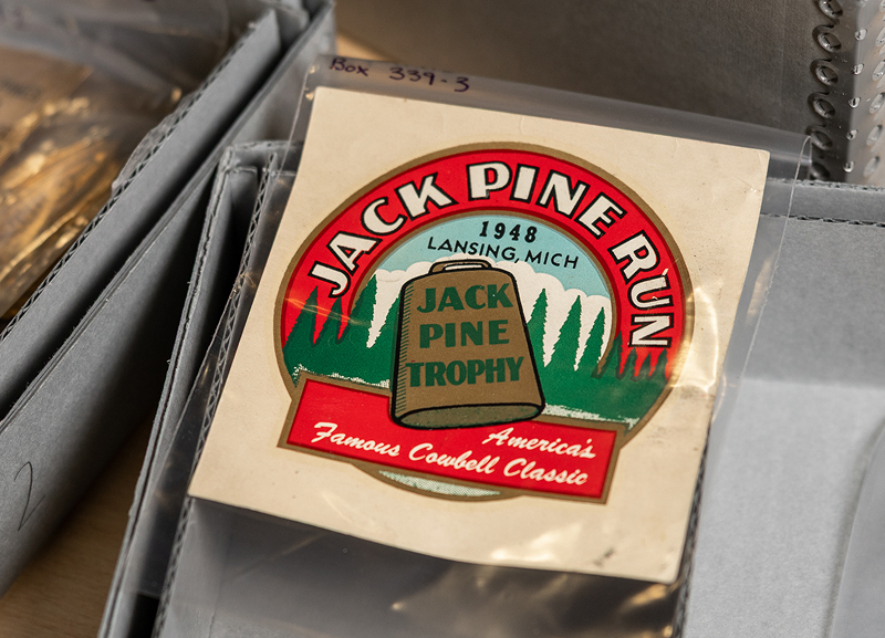 Archival Jack Pine Run sticker from 1948 displayed in a sleeve, featuring trees and bold lettering