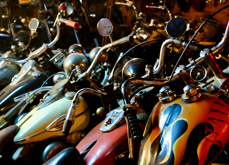 Close view of multiple custom motorcycles lined closely together, showing handlebars, mirrors, and painted fuel tanks