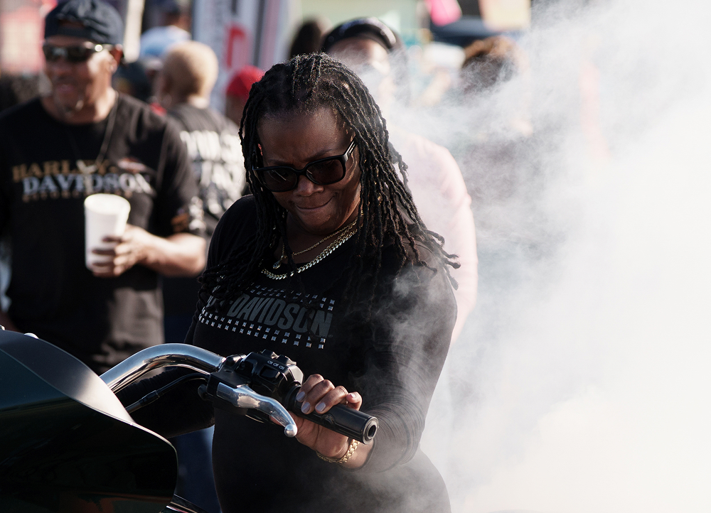 Motorcycle rider grips the handlebars as smoke rises around the bike during a crowded outdoor event