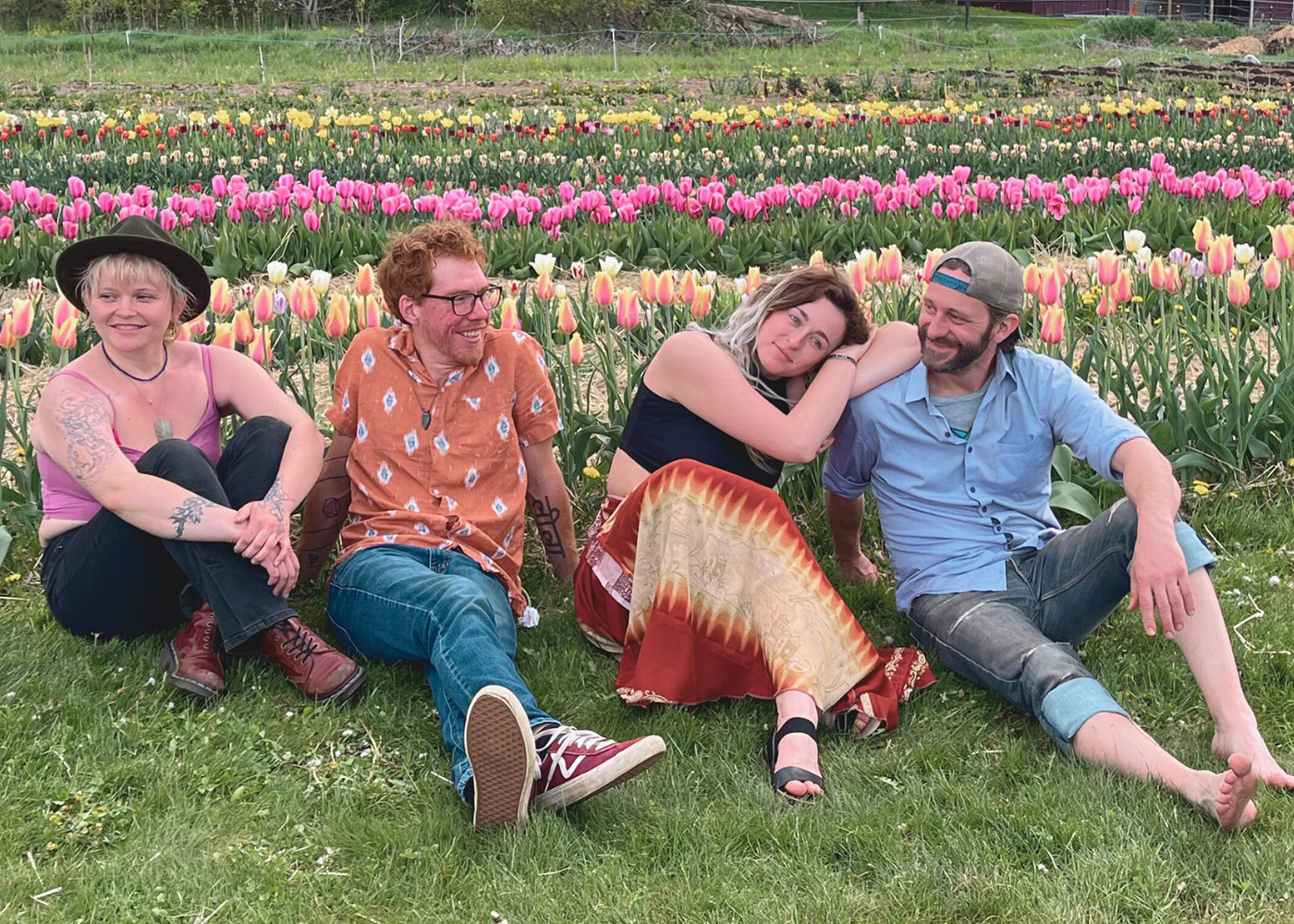 Group of four people sitting in a flower field with colorful blooms
