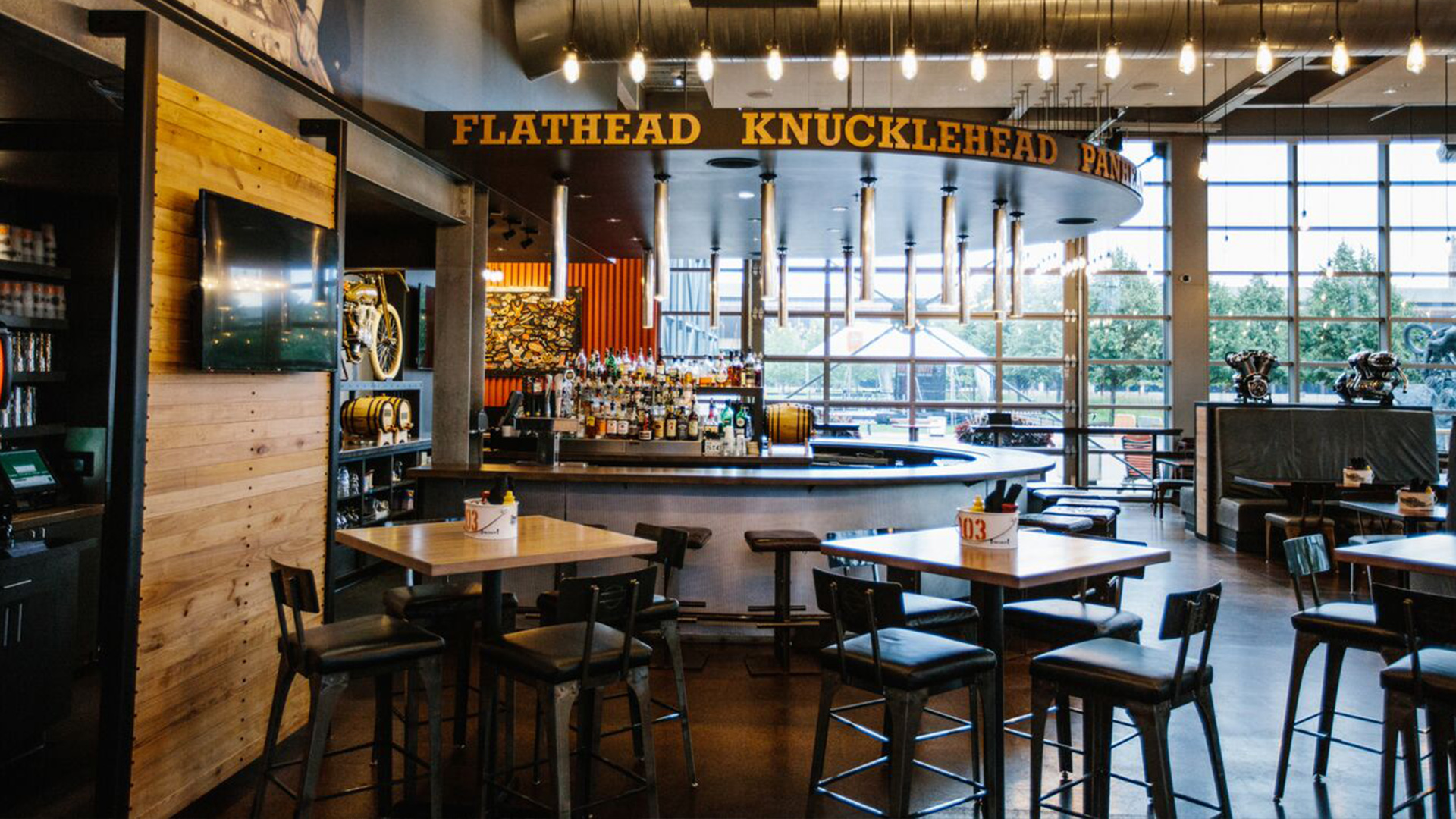 Bar seating area with tables, stools, and overhead signage in Harley-Davidson themed space
