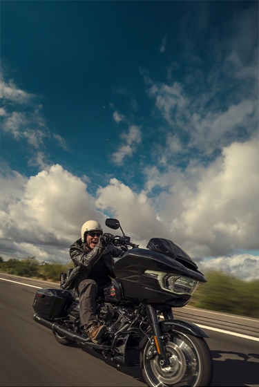 Smiling rider on a black touring motorcycle traveling at speed on an open highway.