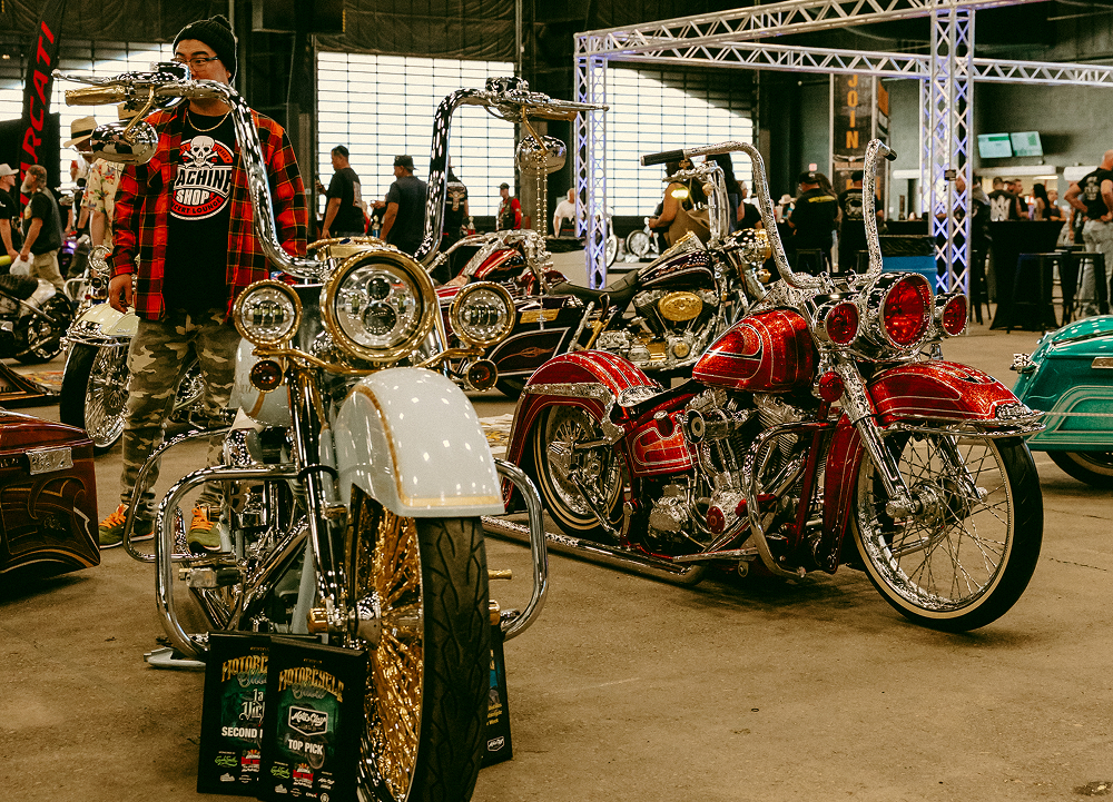 Display of custom chopper motorcycles parked indoors with chrome details under bright event lighting.