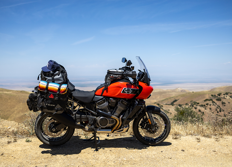 Red H-D Pan America motorcycle with full luggage parked on dusty overlook with rolling hills and clear sky