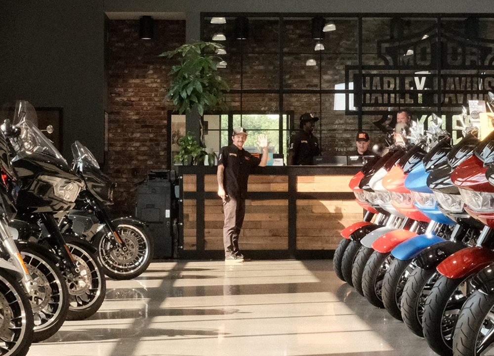 A dealership employee waves at the end of rows of Harley-Davidson motorcycles lining the showroom floor