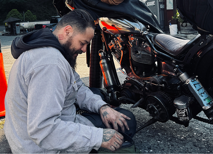 Close-up of Christian Sosa kneeling beside hand-built 1976 Shovelhead, adjusting components near the rear wheel and engine area