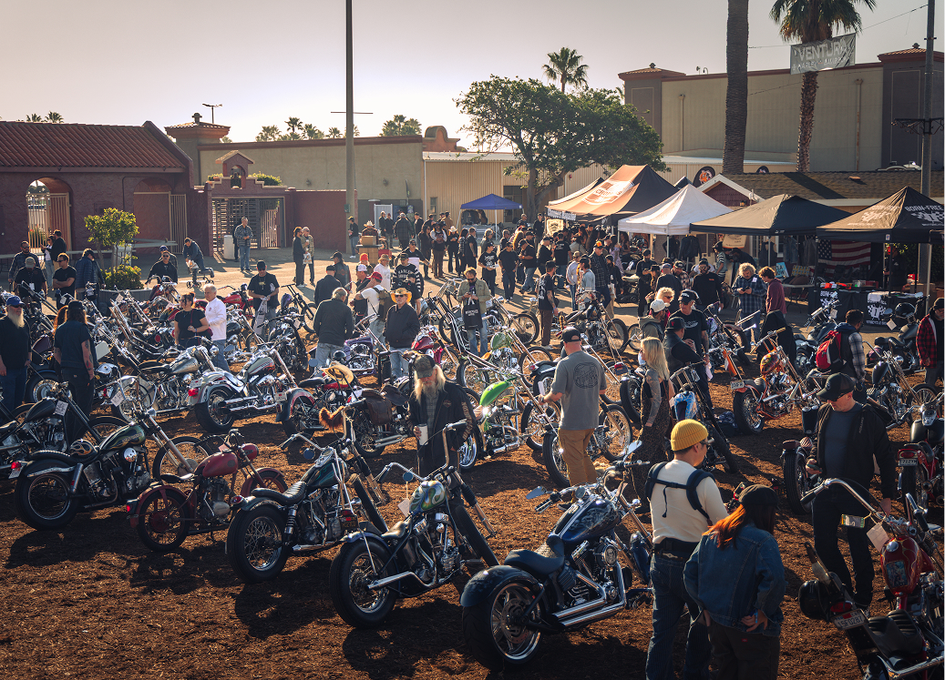 Wide shot of a large outdoor motorcycle show with rows of custom bikes and crowds walking among vendor tents