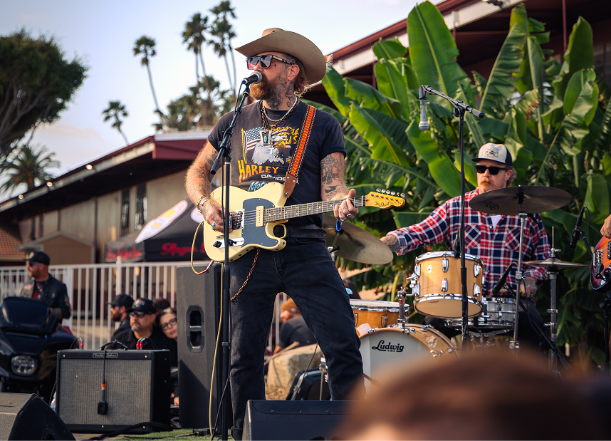 Musician performing on an outdoor stage with a band during a motorcycle event