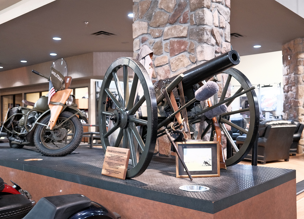 Historic cannon and motorcycle exhibit displayed on a raised platform inside the Bumpus Harley-Davidson showroom