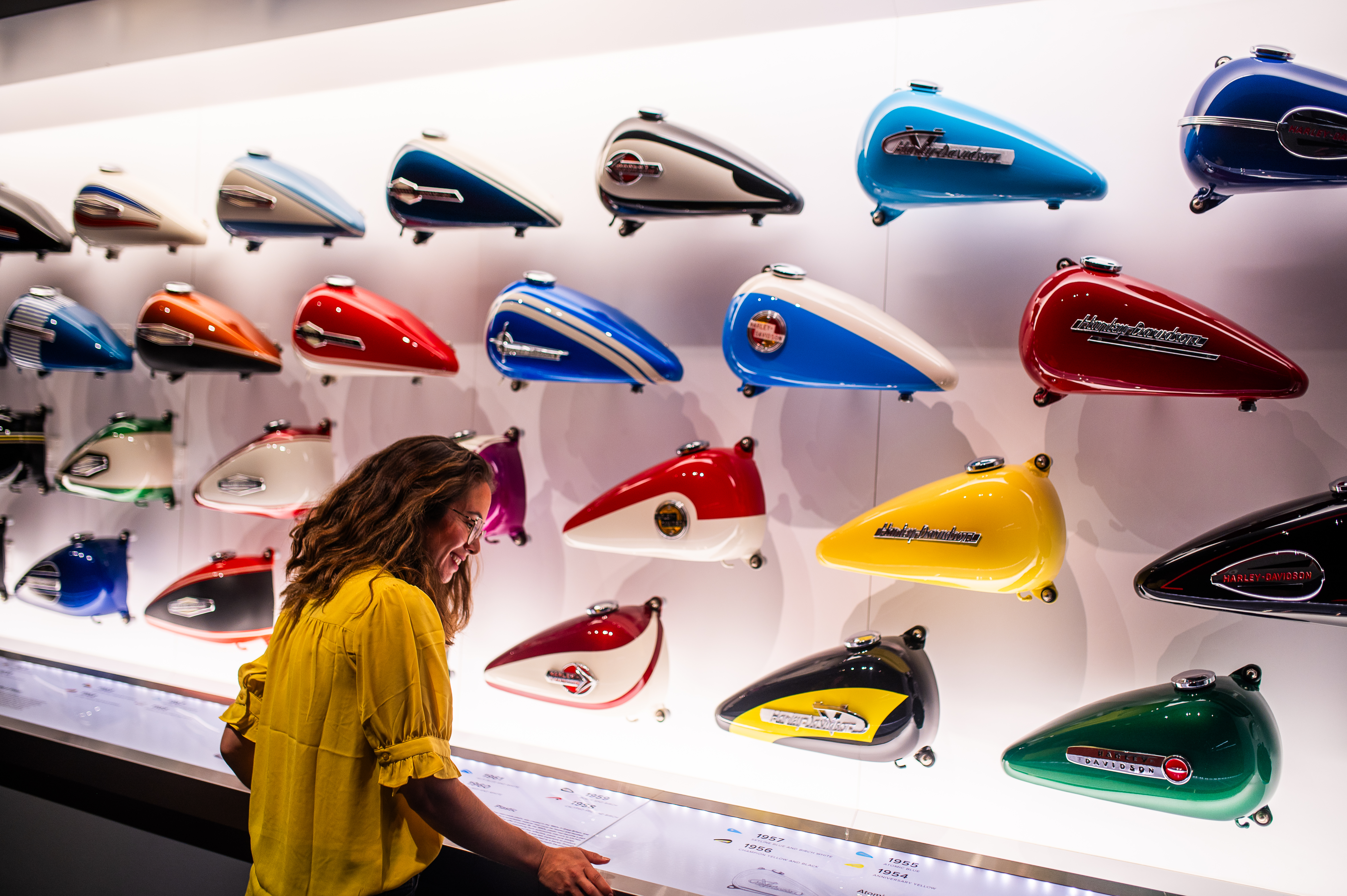博物館でカラフルなハーレーダビッドソンのフューエルタンク展示を見学する来館者