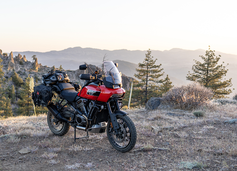 Red H-D Pan America motorcycle with luggage parked on rocky overlook with pine trees and distant mountains