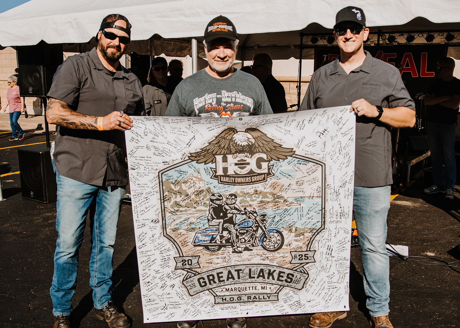 Three people holding a large signed banner for the 2025 Great Lakes H.O.G. Rally in Marquette, MI
