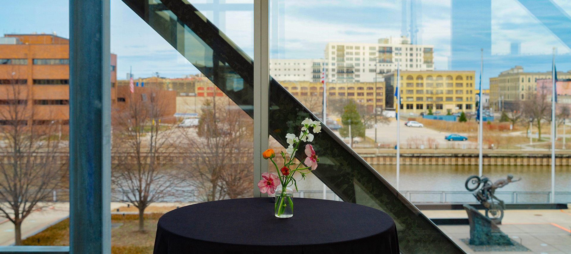 Cocktail table with flower vase near window overlooking river and city buildings