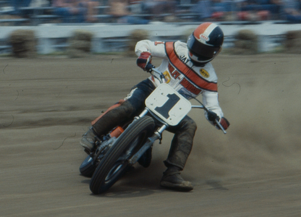 Number 1 rider Jay Springsteen slides a Harley-Davidson flat track motorcycle through a dirt corner as dust flies before spectators