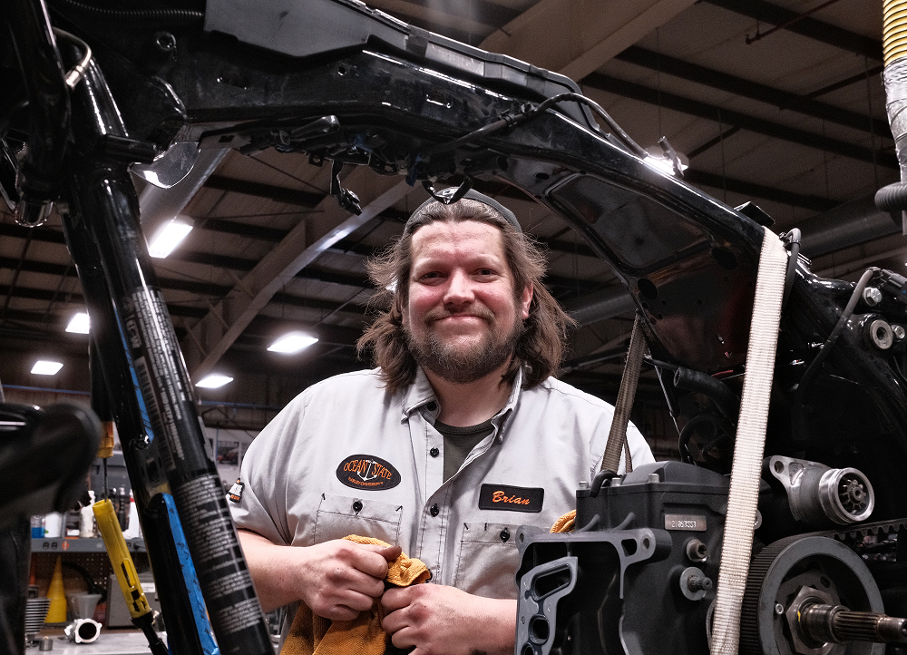 Harley-Davidson technician working on stripped motorcycle frame inside workshop with tools and lift