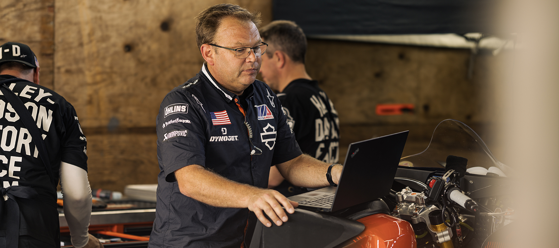 Harley-Davidson Factory Racing Lead Crew Chief Bjorn Christensen works intently at a laptop that is sitting on top of a race bike.