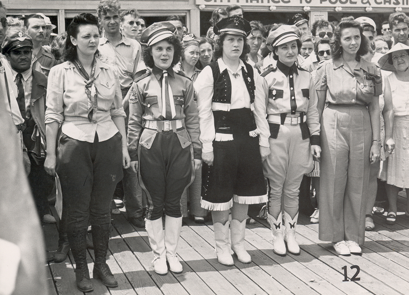 Archival photograph of motorcycle club members in coordinated uniforms gathered on a boardwalk