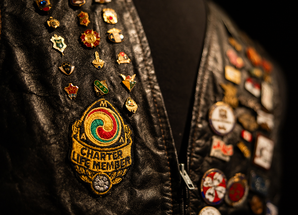 Close-up of black leather vest covered in pins, featuring a colorful embroidered Charter Life Member AMA patch