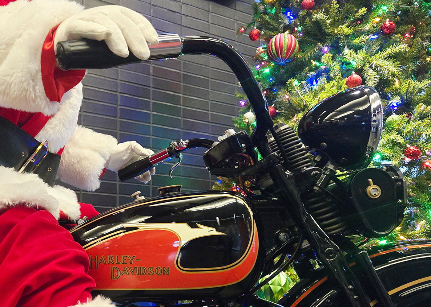 Santa riding vintage Harley-Davidson motorcycle beside decorated Christmas tree