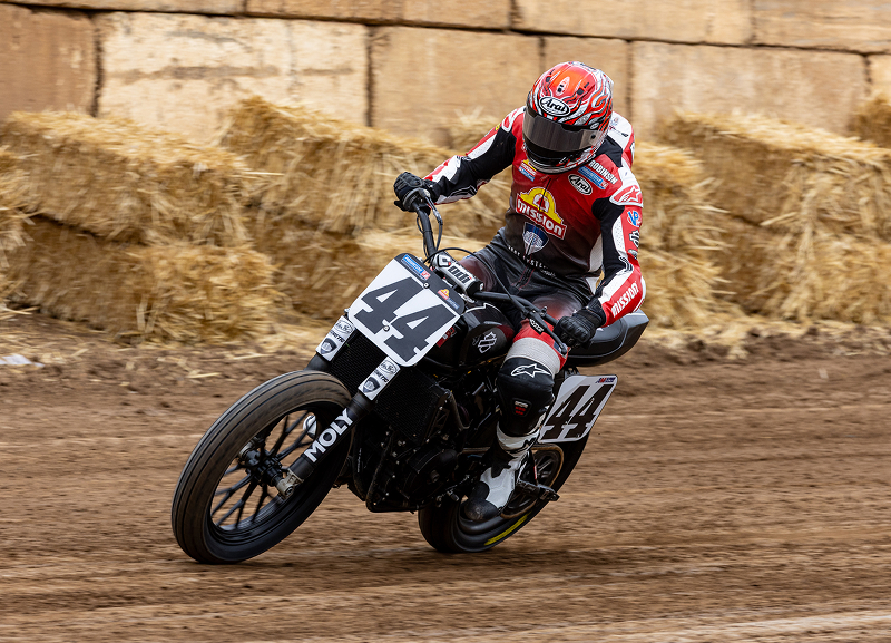Brandon Robinson rides motorcycle #44 through a dirt-track corner, kicking up dust beside hay bales