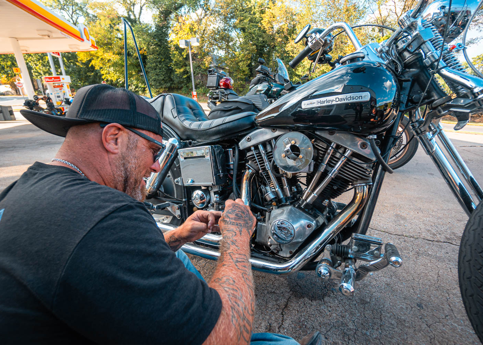 A man tinkers with his bike in a gas station parking lot