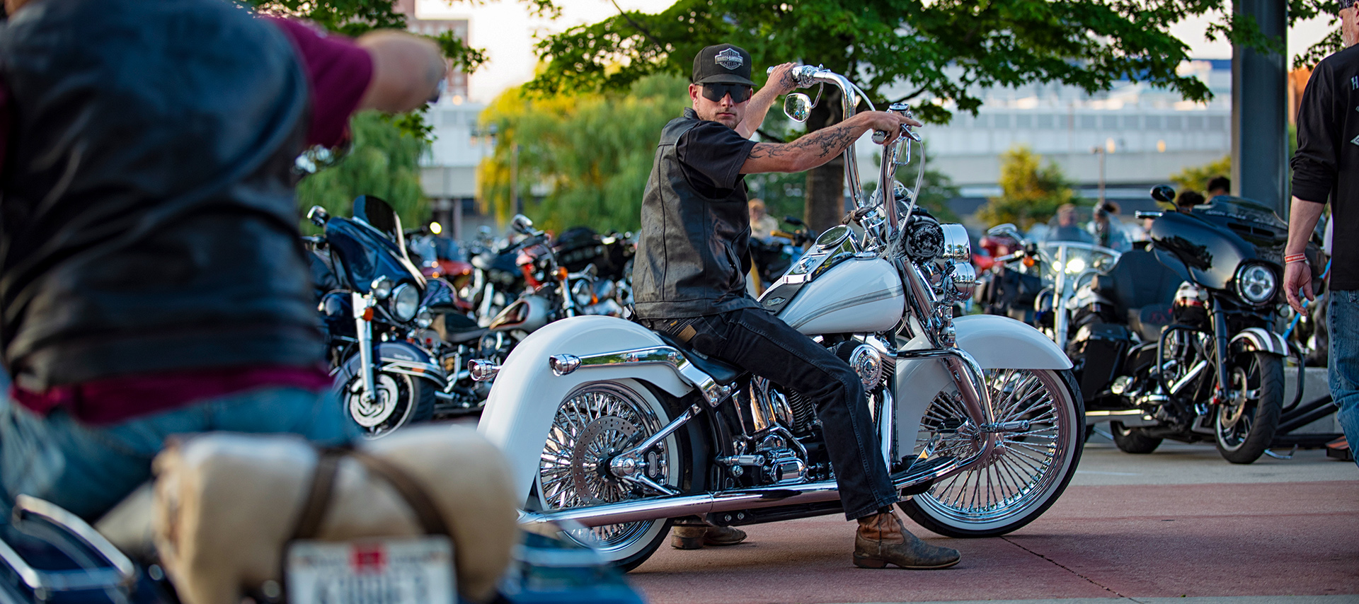 屋外のバイク集会で、ハンドルバーを高くしたカスタムHarley-Davidsonのオートバイに乗る人物