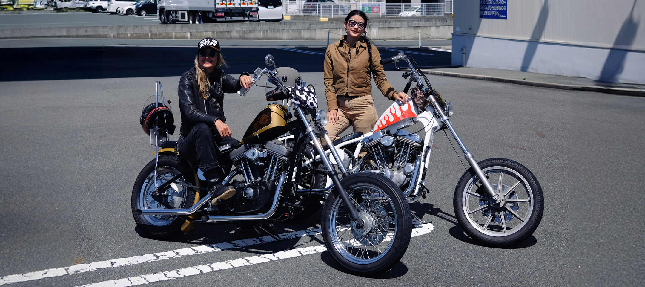 Two custom choppers parked side by side in a parking lot with the authors posing beside them in bright daylight