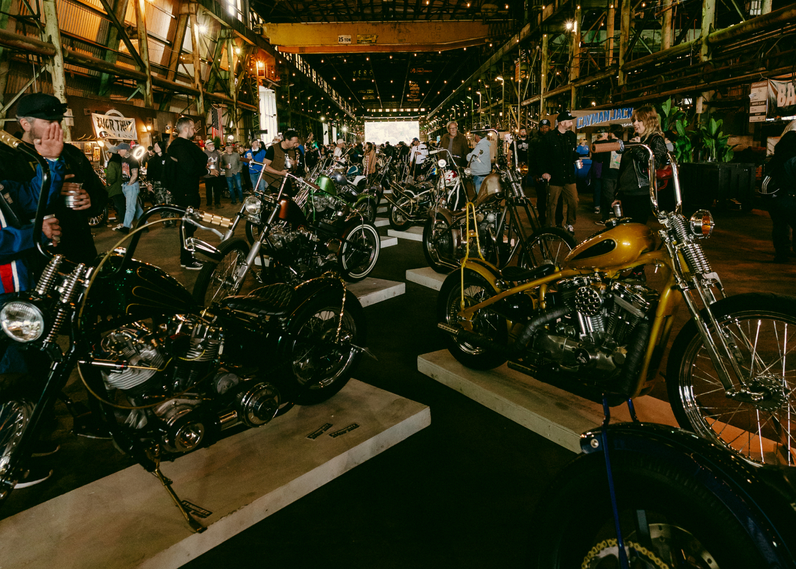 Two rows of bikes for viewing, one on the left and the other on right, lead down the middle of the building, with dozens of people walking on either side admiring the bikes. 