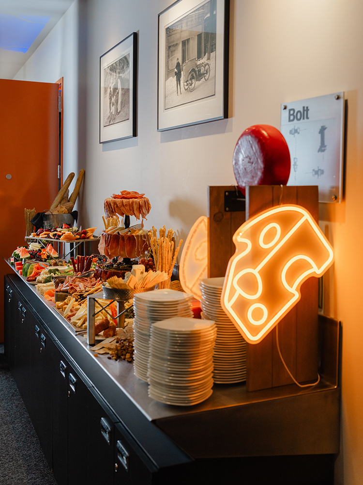 Snack buffet with chips, plates, and neon cheese sign on table