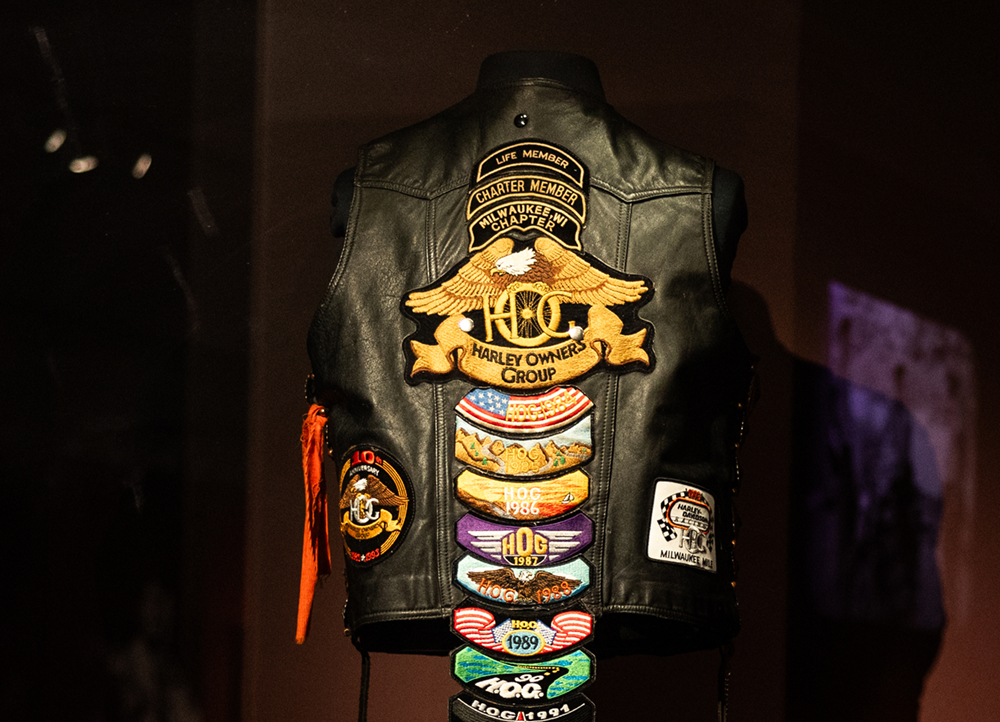 Back view of a black leather with a long column of Harley Owner’s Group patches running down the center and out of frame