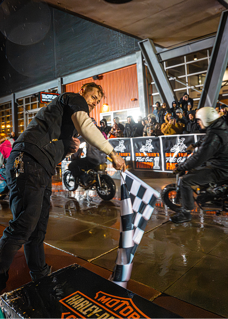 Event staff waves a checkered flag as a motorcycle approaches the finish area on a rainy track