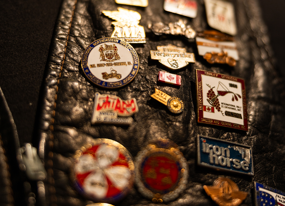Close-up of a black leather vest covered with assorted metal pins and badges, showing varied designs and colors