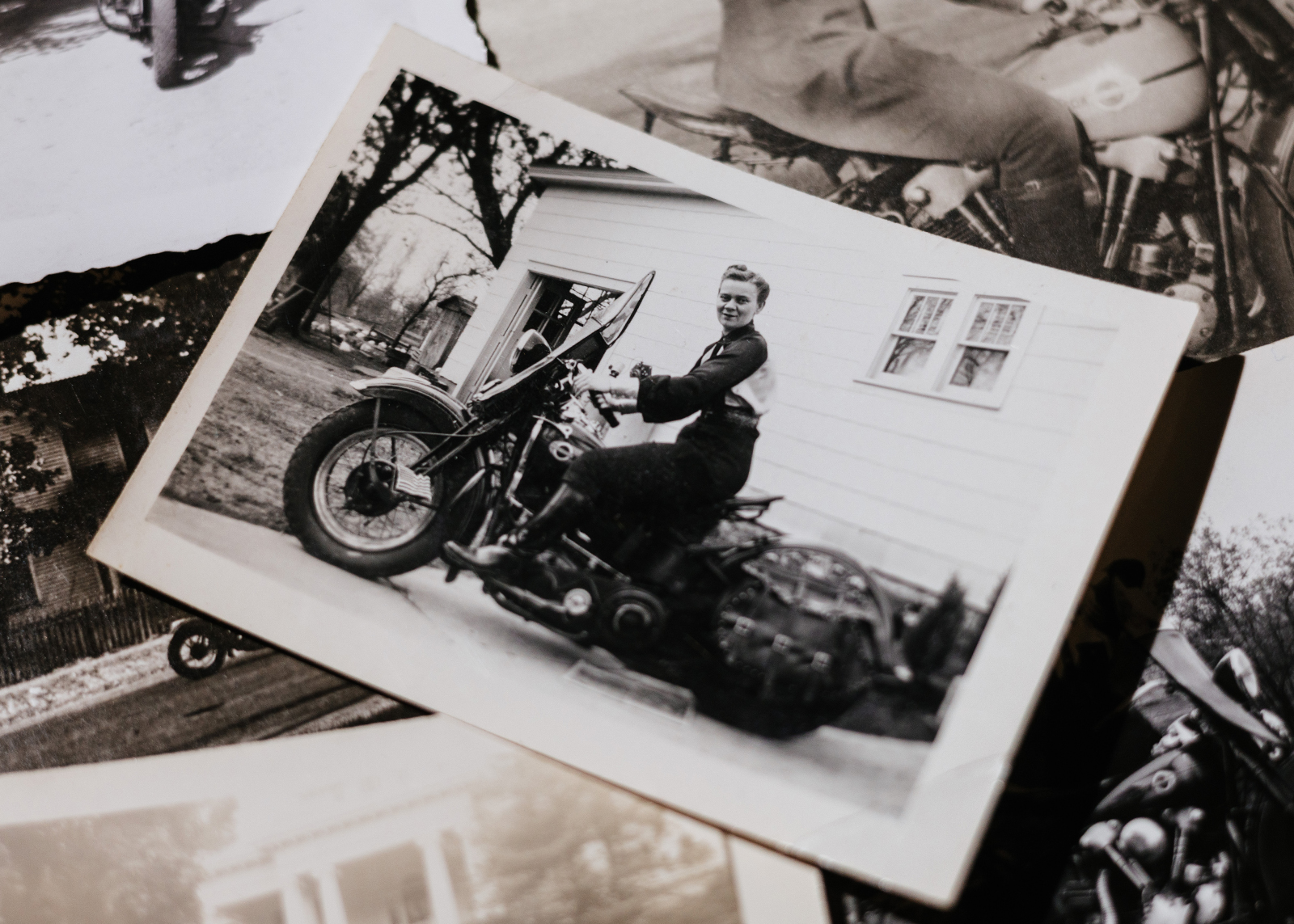 A photo of a vintage Motor Maid photo showing a woman sitting on her motorcycle in front of a house, surrounded by other vintage photos.