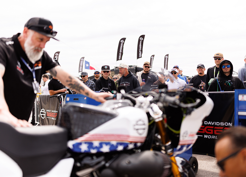 Crowd gathers around a custom Harley-Davidson race bike during a live motorcycle showcase event