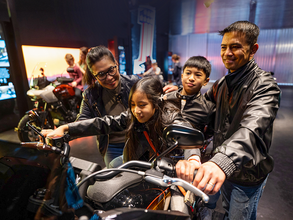 Family exploring interactive Harley-Davidson motorcycle exhibit indoors