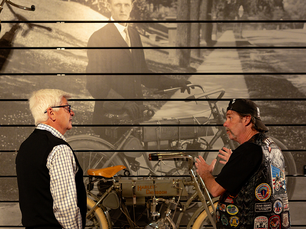 Two visitors discussing vintage Harley-Davidson motorcycle in front of historic mural