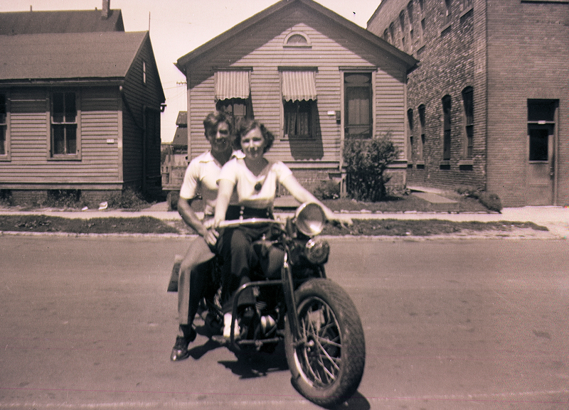 Gustaf Stenmark and Elsi Toplak on a motorcycle on a residential street, centered between small houses and buildings