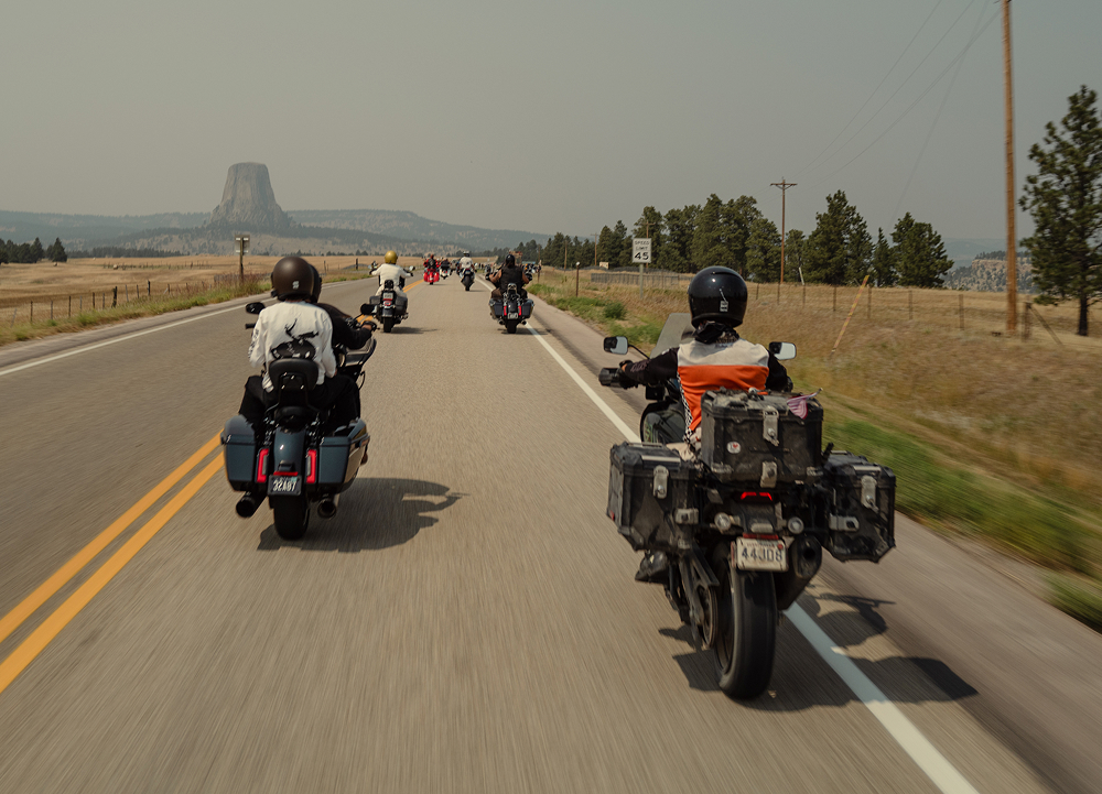 Group of motorcycles rides along a Wyoming highway toward Devils Tower rising in the distance