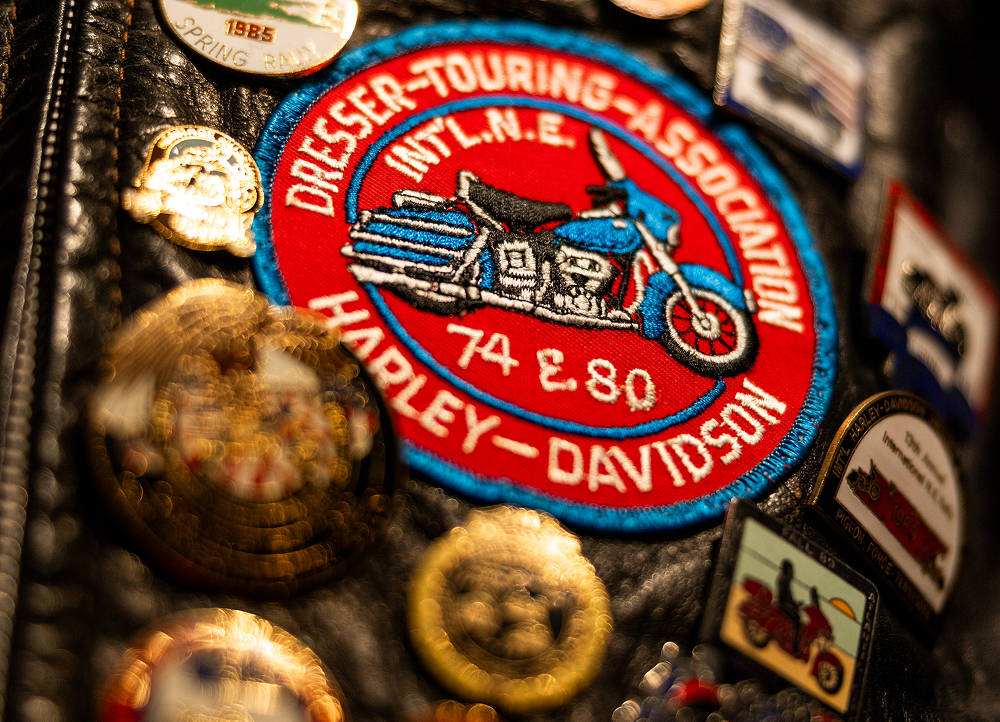 Close-up of a Harley‑Davidson touring patch and vintage pins attached to worn black leather