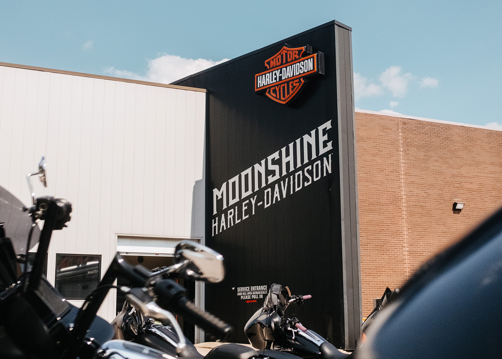 Looking up at the exterior signage of Moonshine Harley-Davidson dealership with motorcycles in the foreground.