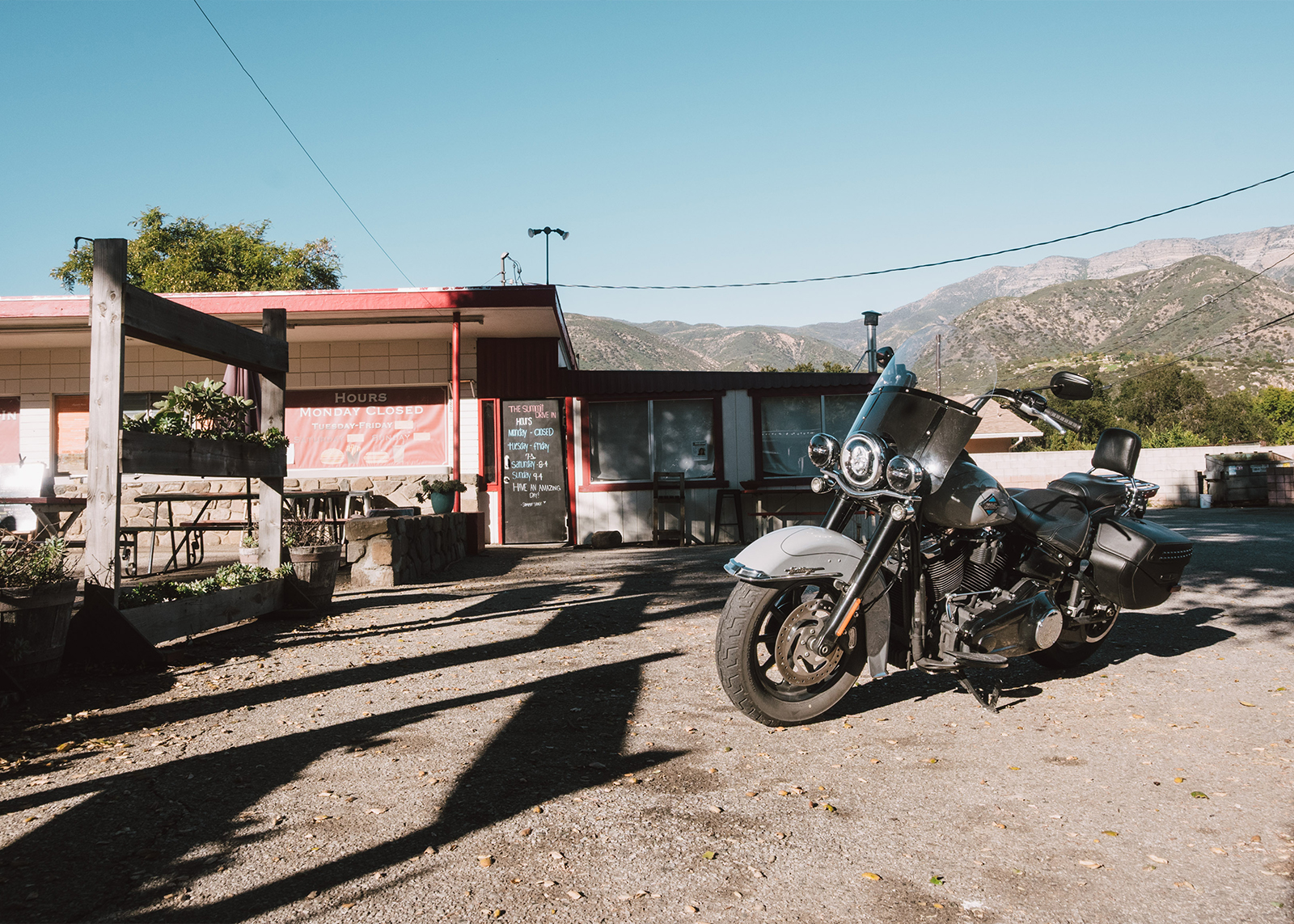 A Harley-Davidson Heritage Classic motorcycle parked outside a rustic roadside diner with mountains visible in the background