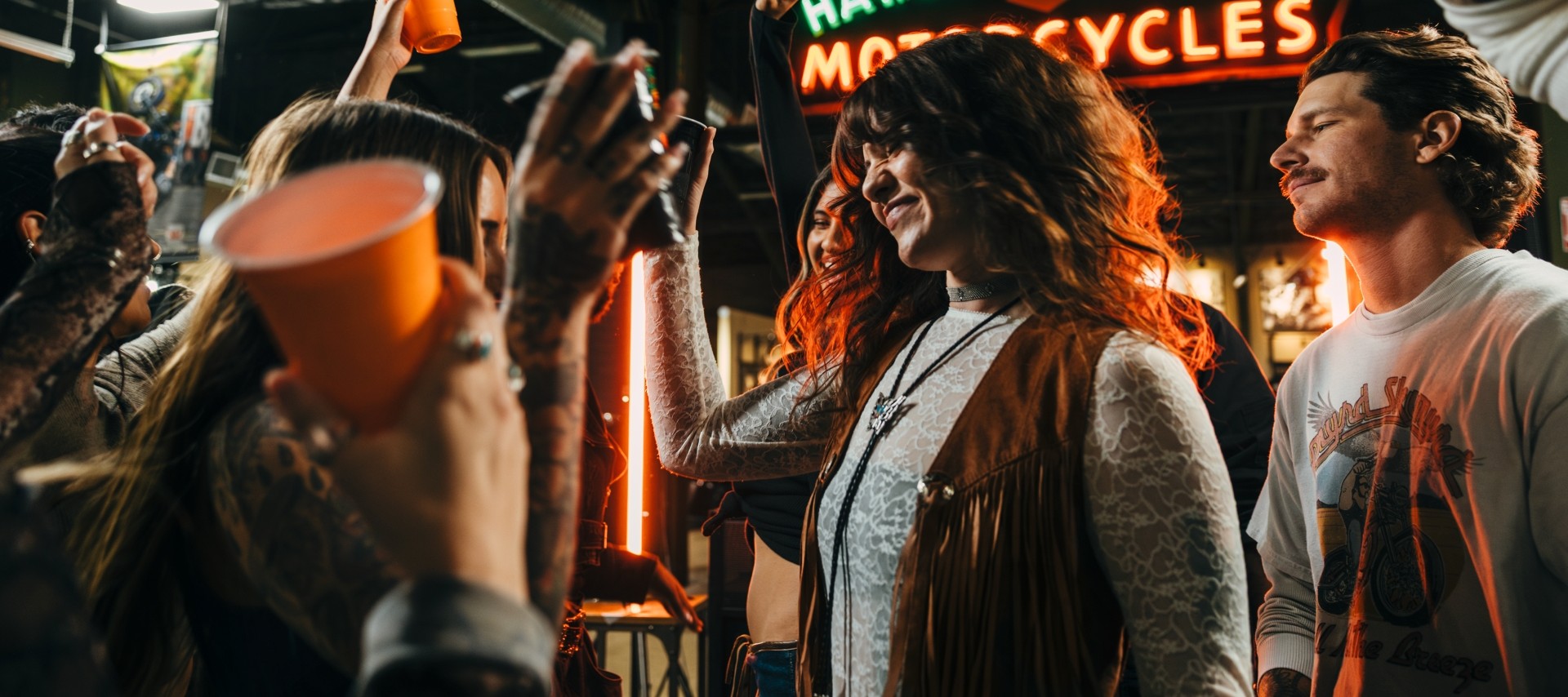 Gruppo di persone che balla e alza i bicchieri per brindare durante un evento delle Harley Nights al chiuso.