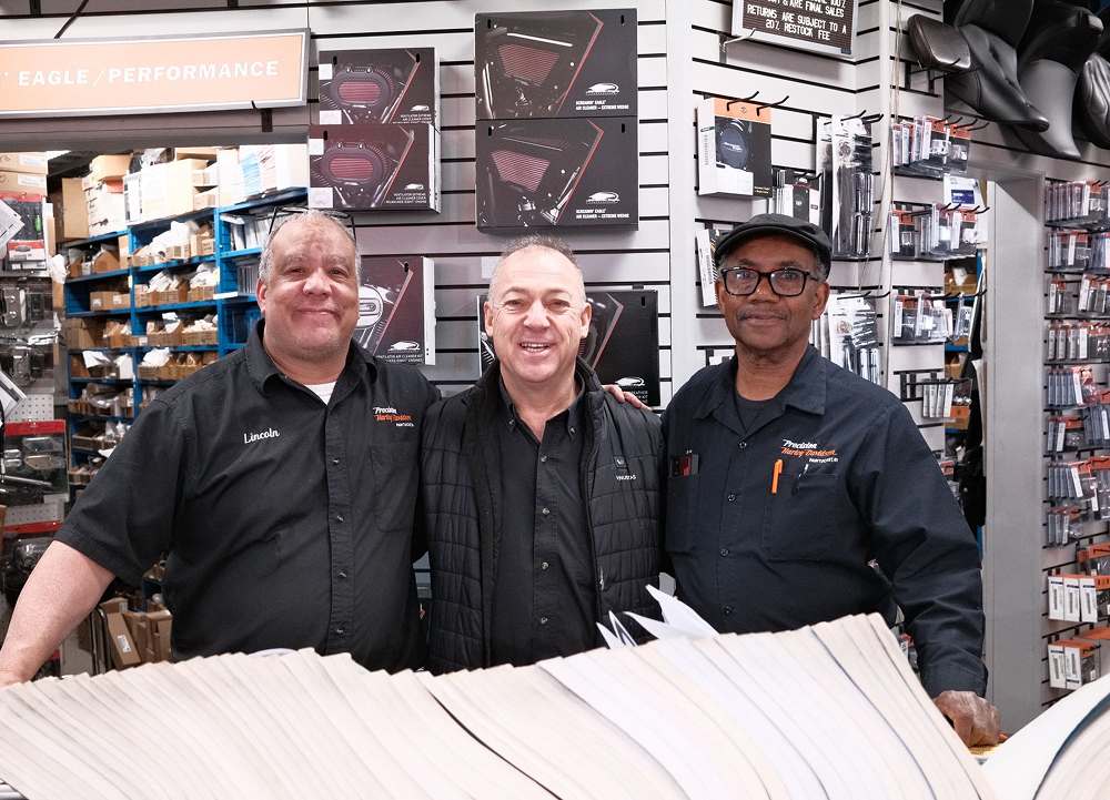 Richie Pilavin poses with 2 coworkers behind a desk at Precision H-D