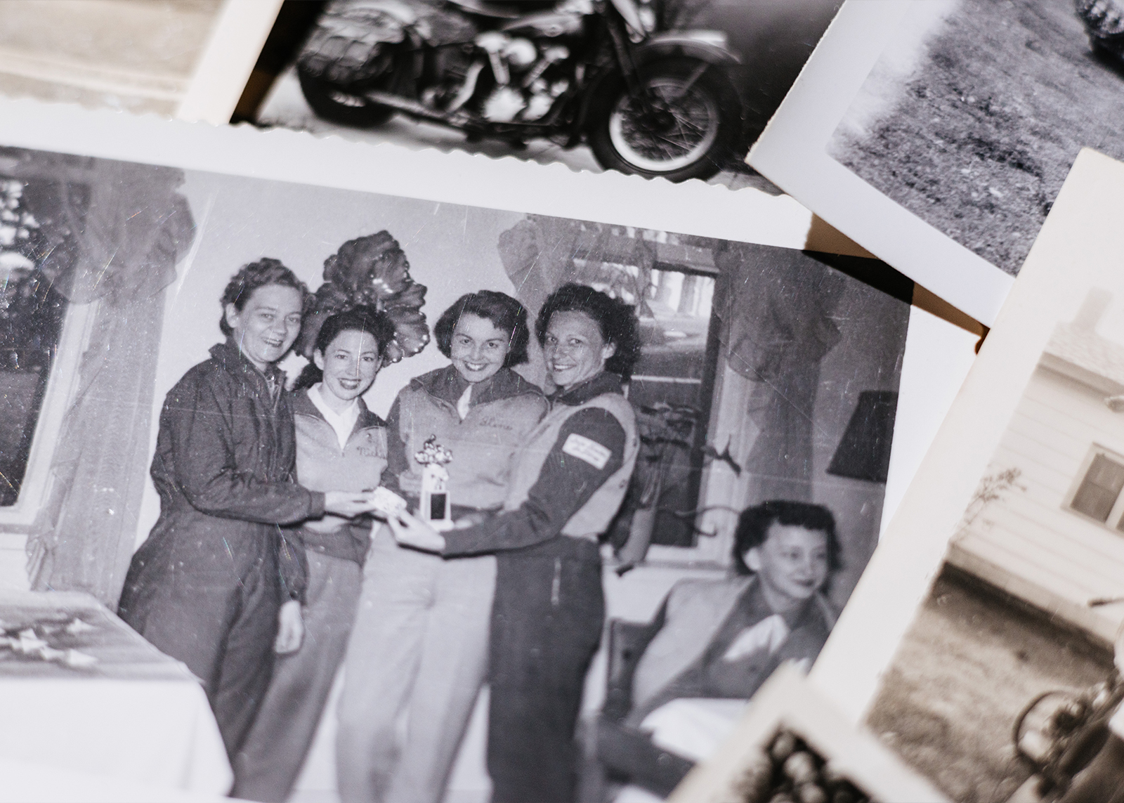 A photo of a vintage Motor Maid photo showing members gathered in a living room holding a motorcycling trophy.