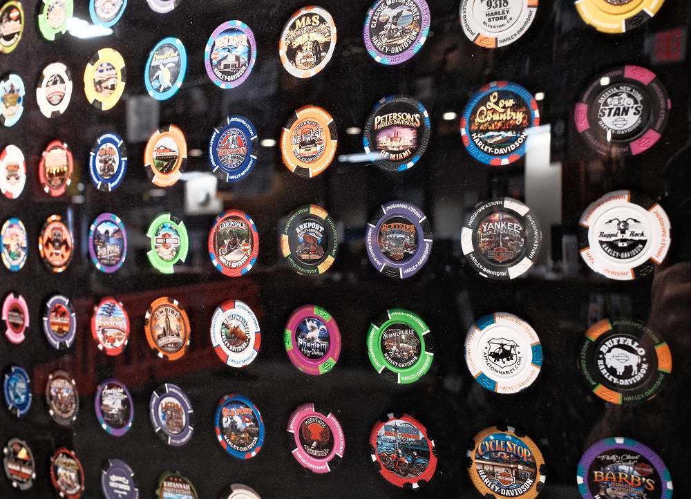 Close-up display of colorful Harley-Davidson challenge coins and poker chips mounted on dark wall