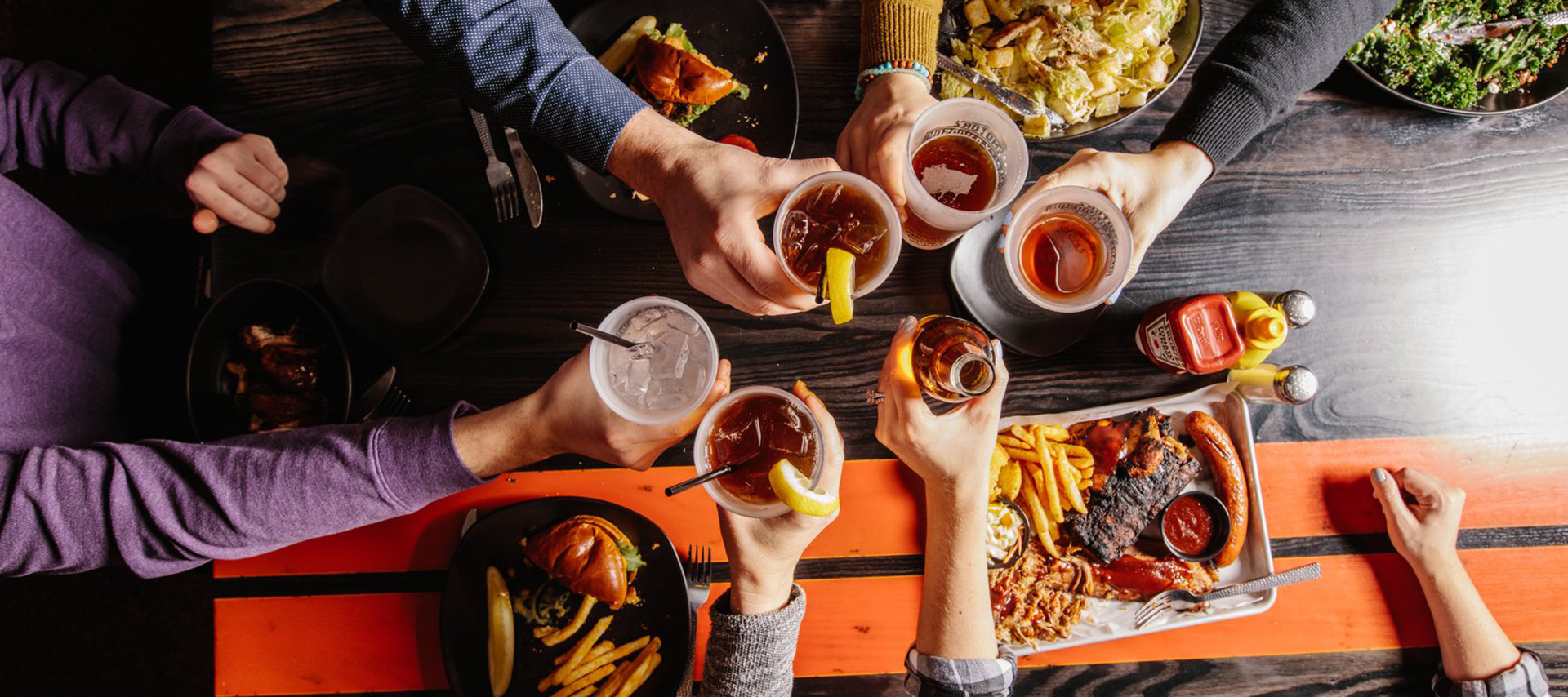 テーブルを囲んでバーベキュー料理と付け合わせを前に飲み物で乾杯する人々