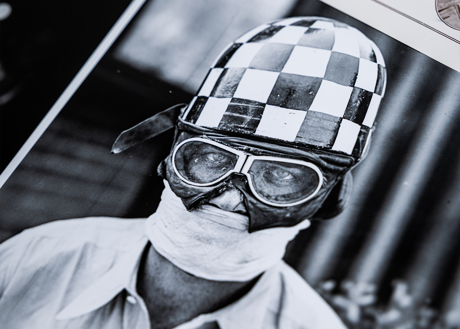 Photo of an archival black and white image of a rider wearing a checkered helmet, goggles, and face covering.