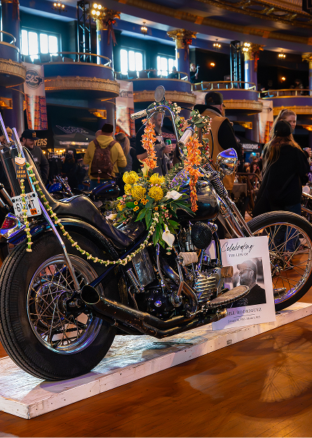 Custom motorcycle on display memorializing Bill Rodriguez, with detailed chrome parts and flowers arranged on the seat