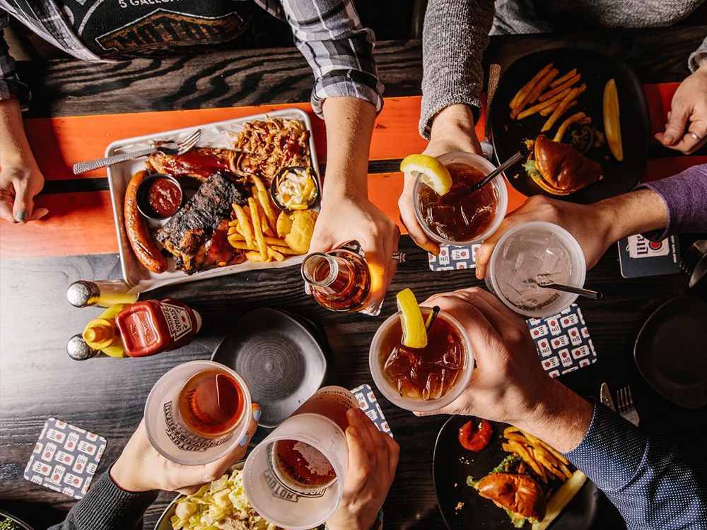 Group toasting drinks over table with barbecue platter and sides