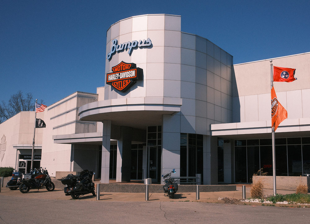 Exterior of Bumpus Harley-Davidson dealership with modern facade, logo signage, and flags under blue sky